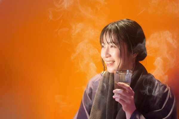 専用マントに包まれ、立ちのぼる蒸気に温まる女性